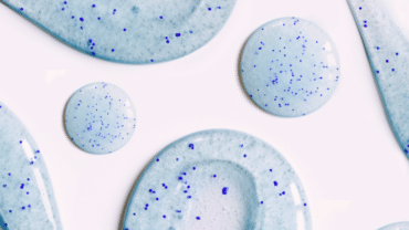 Fundo branco com gotas de produto azulado espalhadas e grãos de microplásticos azul escuro