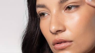 Imagem do rosto de uma mulher. Ela tem a pele morena e os olhos e cabelos escuros. Está com um dedo próximo a um dos olhos, como se estivesse avaliando a vitalidade da sua pele, um dos benefícios do extrato de alga marrom.